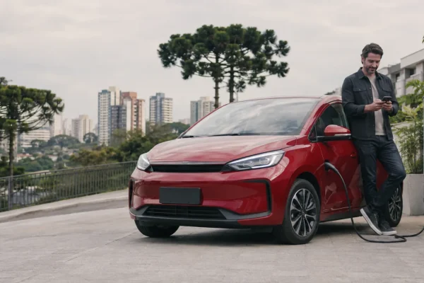Carro elétrico vermelho em recarga residencial em Curitiba enquanto motorista consulta cotação no celular